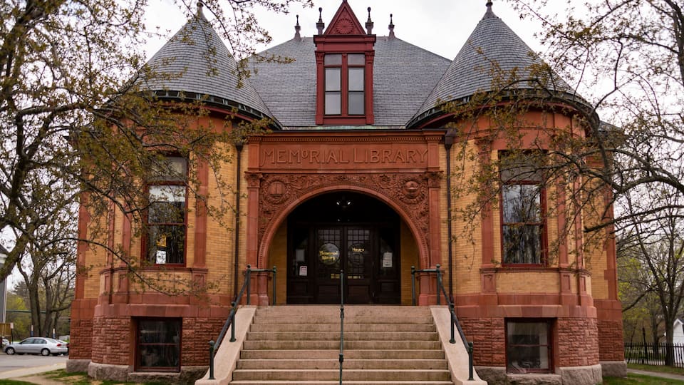A brick building with a central arched entrance, a clock tower, and a red roof.