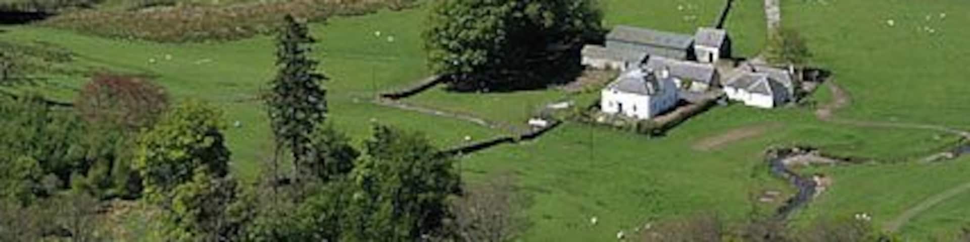 A winding road through a valley with a white house and a small building.