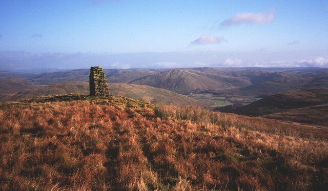 A stone structure on a grassy hill with rolling hills in the background.