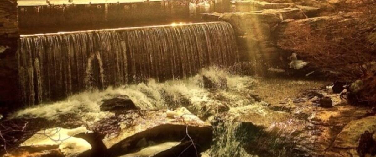 A waterfall cascading over a stone dam in a forested area.