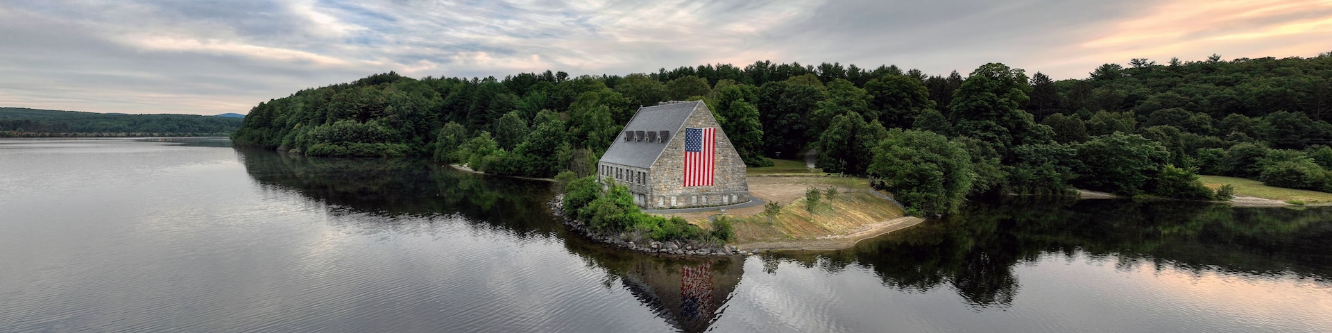 Una casa con una bandera estadounidense junto a un lago rodeado de bosque denso.