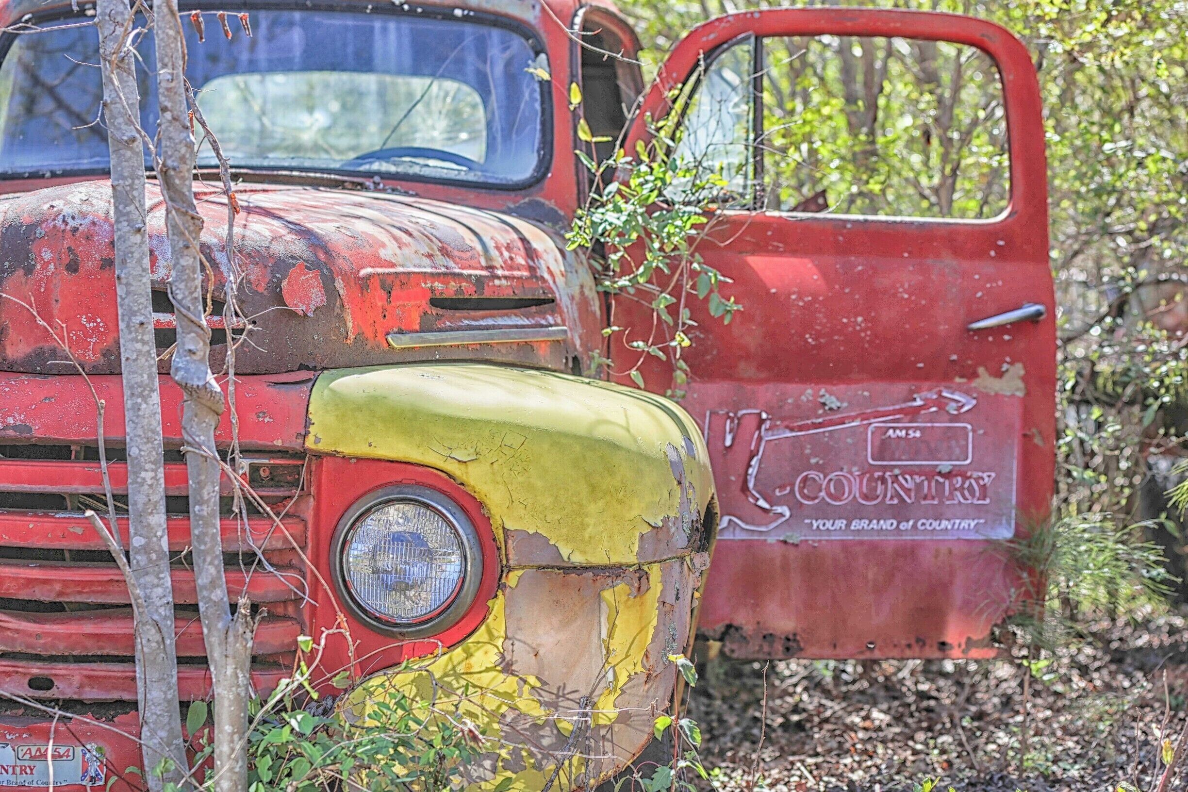 Un camión viejo y oxidado de color rojo, con pintura descascarada y un letrero que dice 'Country'.