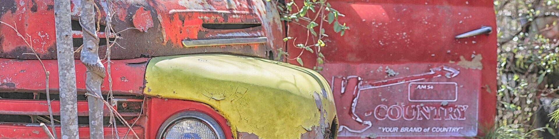 Un camión viejo y oxidado de color rojo, con pintura descascarada y un letrero que dice 'Country'.