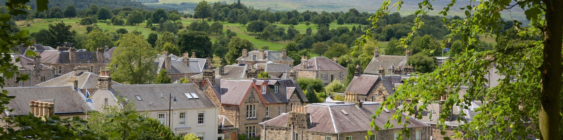 A village with stone houses, a green park, and rolling hills in the background.
