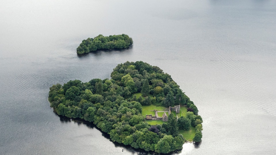 An aerial view of a lake with two small islands, one with a house and a flagpole.
