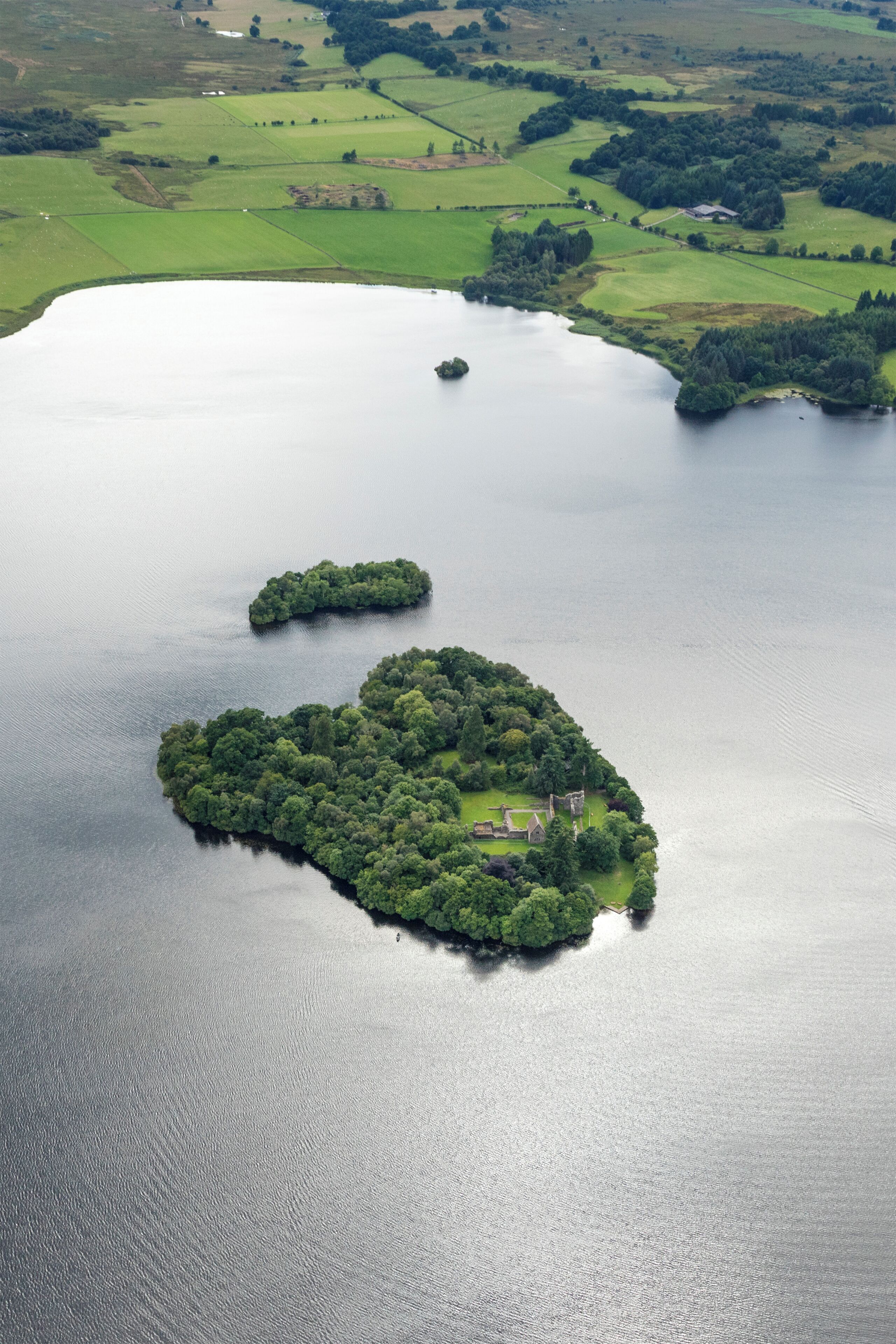 An aerial view of a lake with two small islands, one with a house and a flagpole.