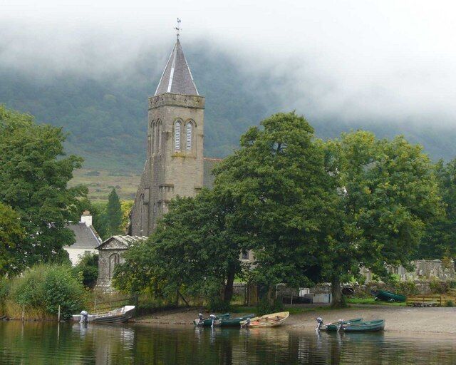 A church with a tall tower by a calm river surrounded by trees.