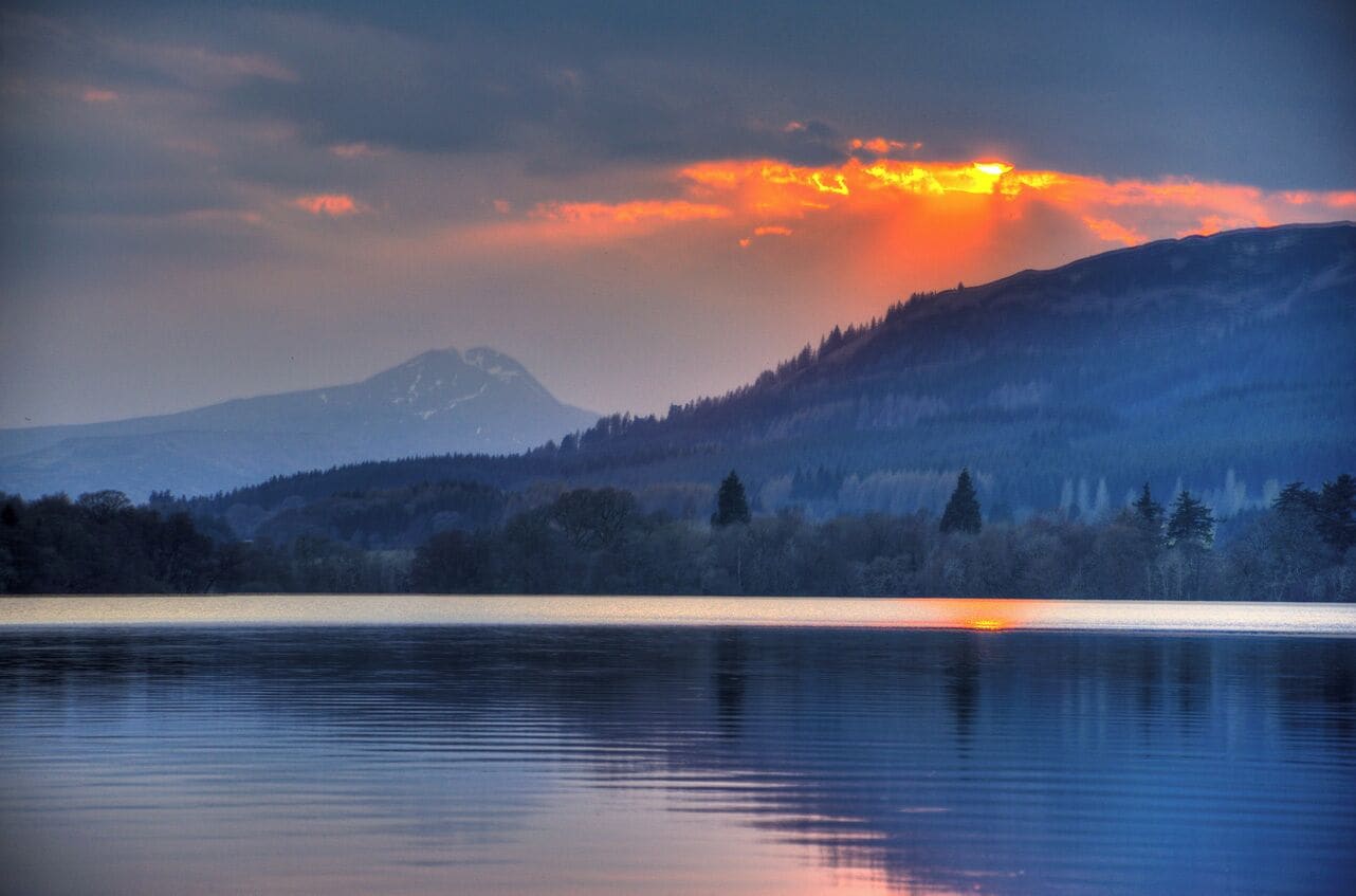 A calm lake with a mountain in the background and a sunset.