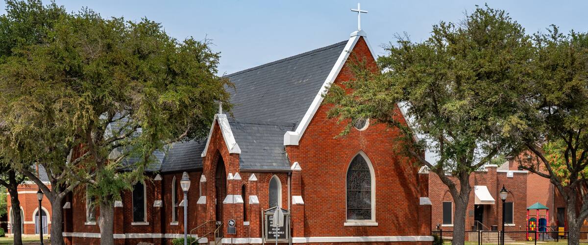 A brick church with a cross on top, surrounded by trees and a paved road.