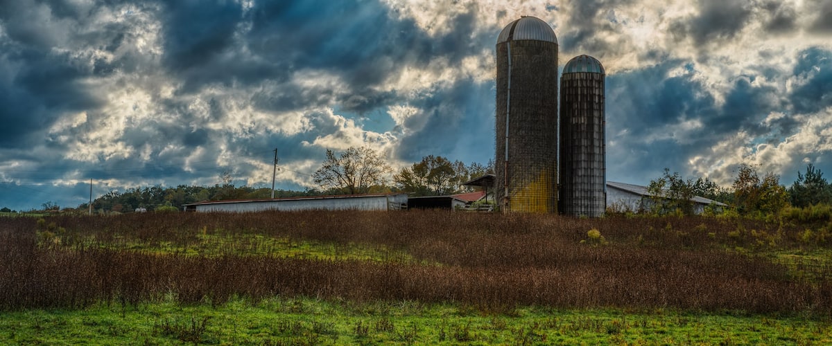 A farm with two silos and a barn under a cloudy sky.