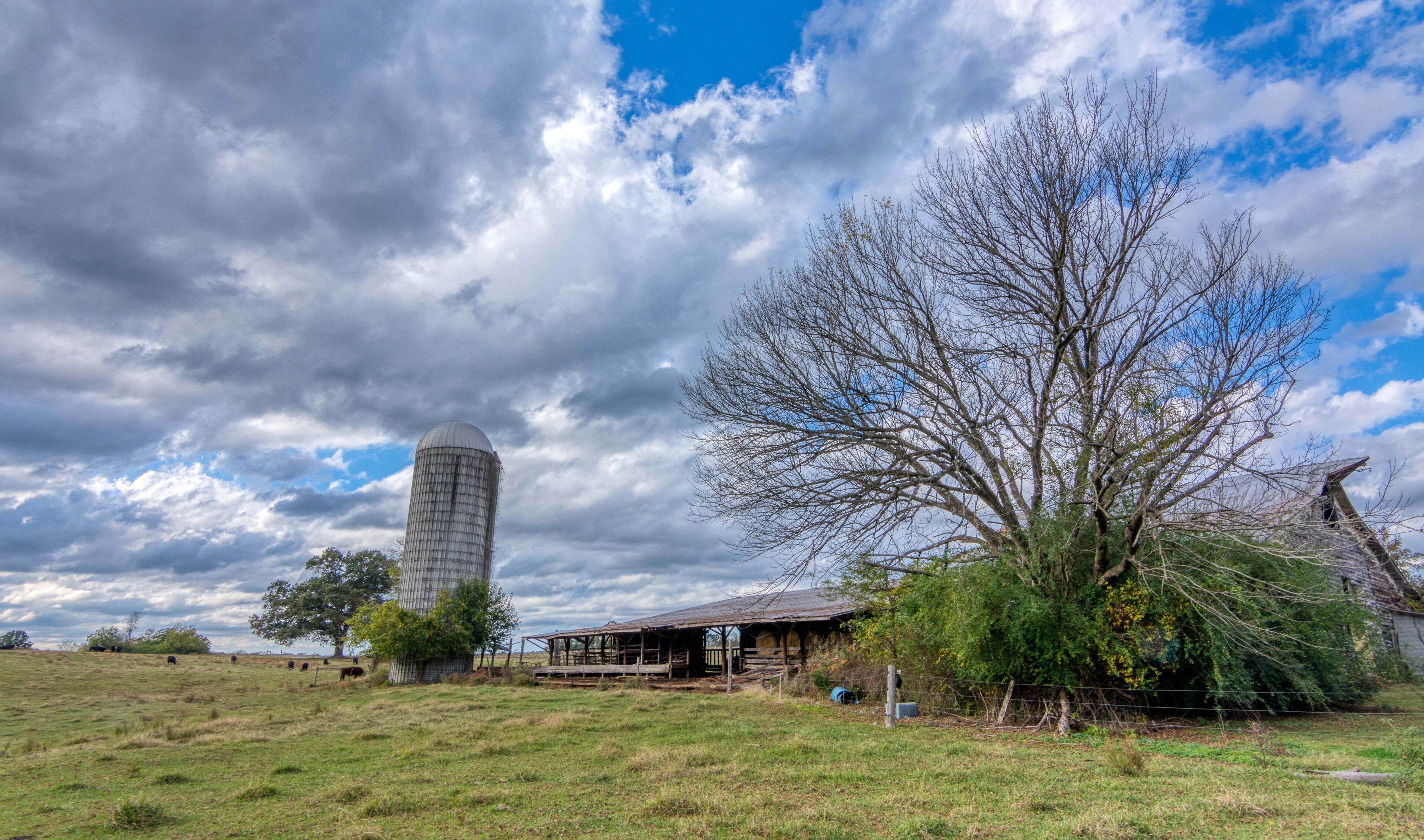 Abandoned barn with silo under stormy clouds