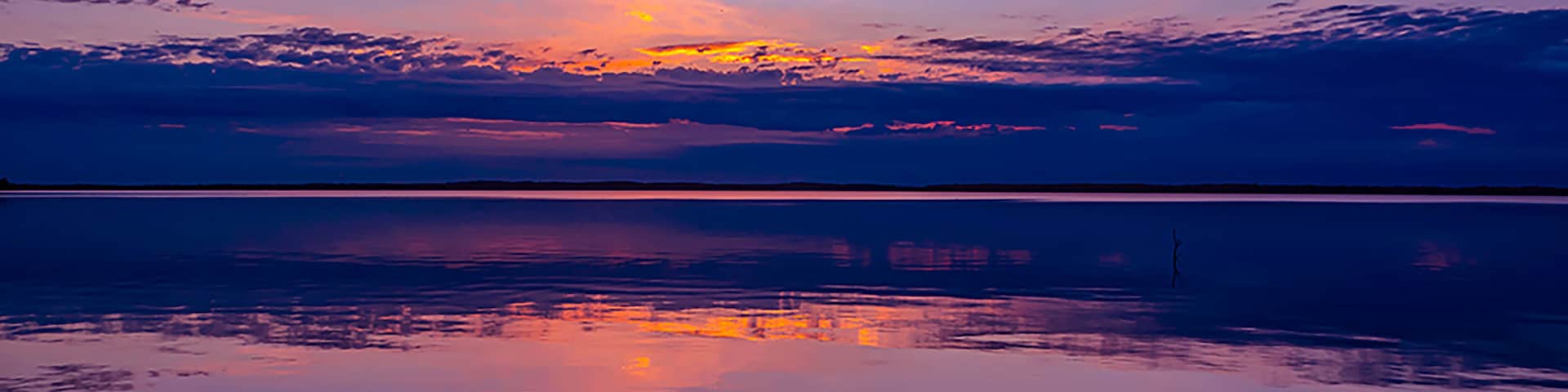 Un atardecer sobre un cuerpo de agua tranquilo, con el reflejo del cielo.