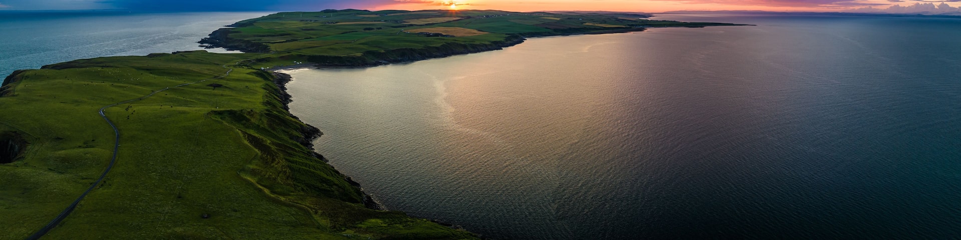 A coastal landscape with a winding road, a body of water, and a sunset.