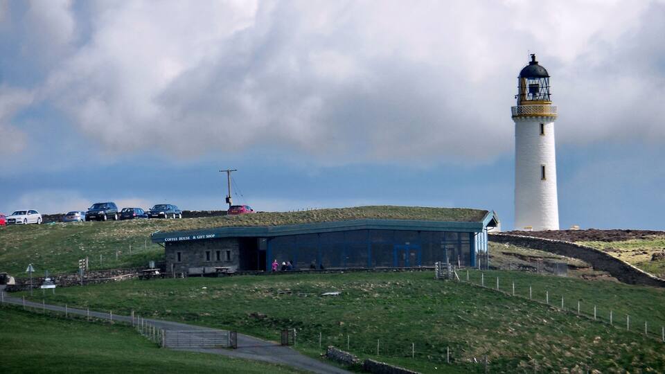 A lighthouse, a coffee house, and a gift shop on a grassy hill.