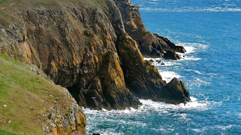A rugged coastline with steep cliffs and a grassy hillside.