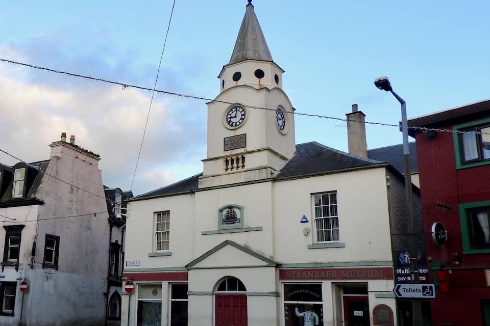 Un edificio histórico con una torre de reloj, un cartel de museo y una puerta roja.