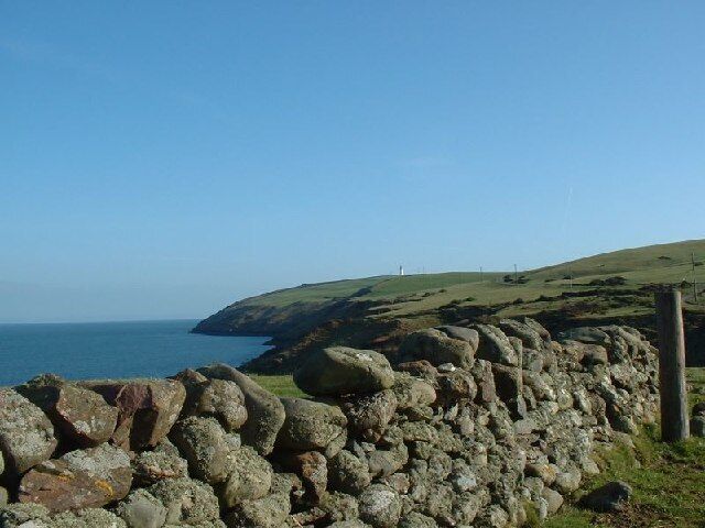 A coastal landscape with a stone wall, grassy hills, and the ocean.