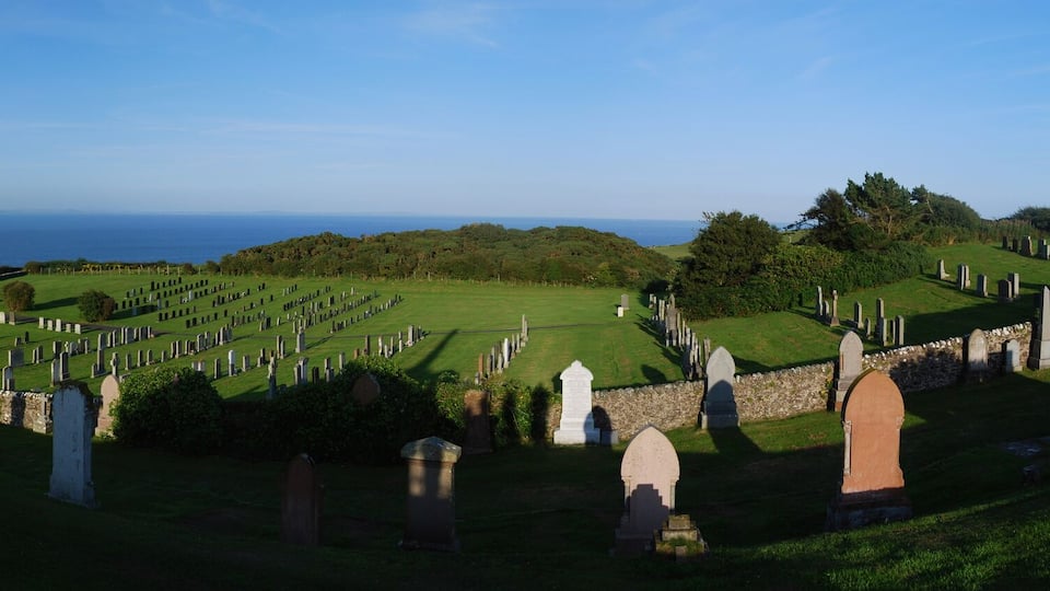 A cemetery with headstones, a church, and a view of the sea.