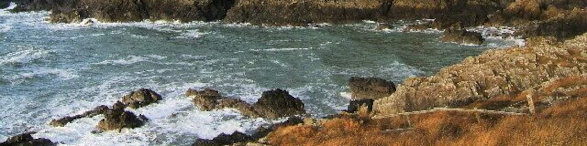 A coastal lighthouse on a rocky outcrop with the ocean in the foreground.