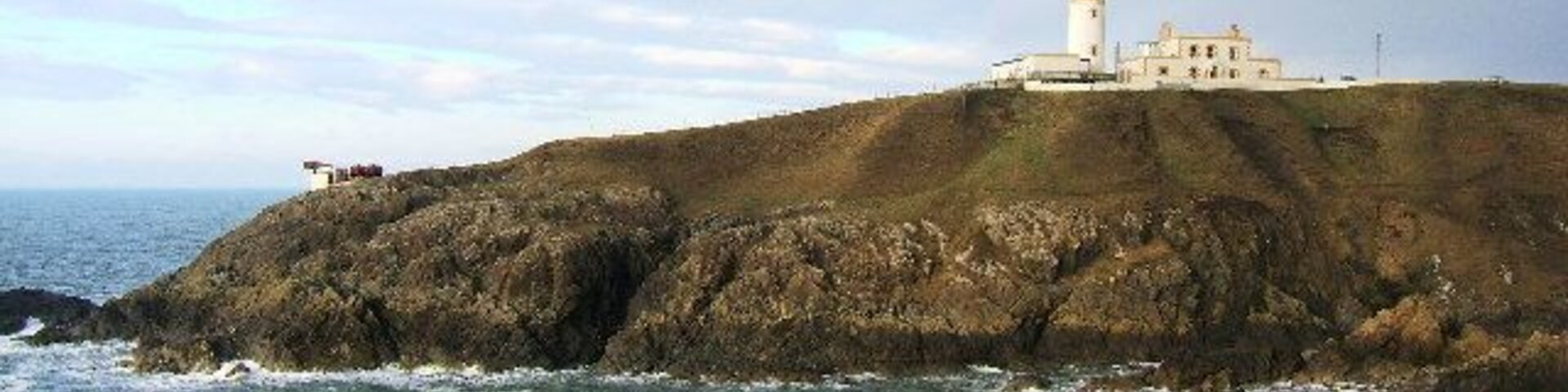 Un faro costero sobre un afloramiento rocoso, con el océano al frente.