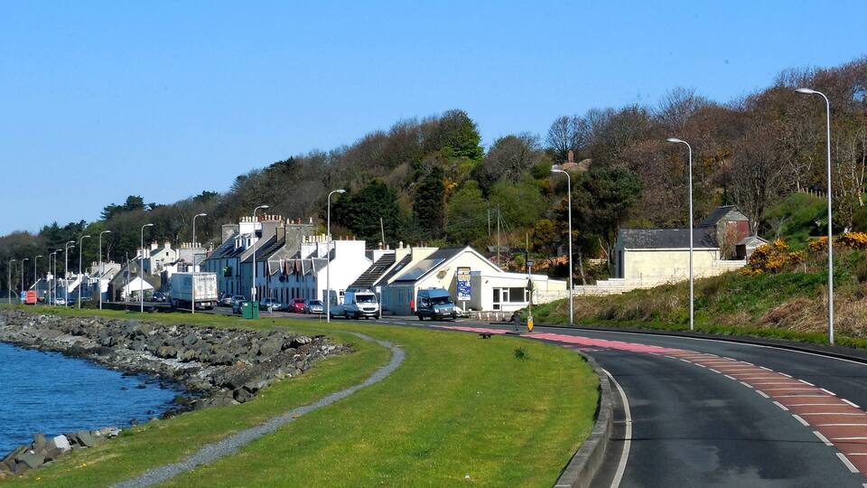 A coastal road with a red bike lane, houses, and a rocky shoreline.
