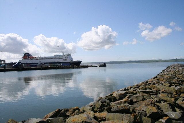 A ferry docked at a rocky pier with calm water and a clear sky.