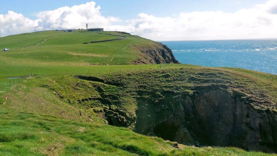 A coastal landscape with a grassy hill, a lighthouse, and the ocean.