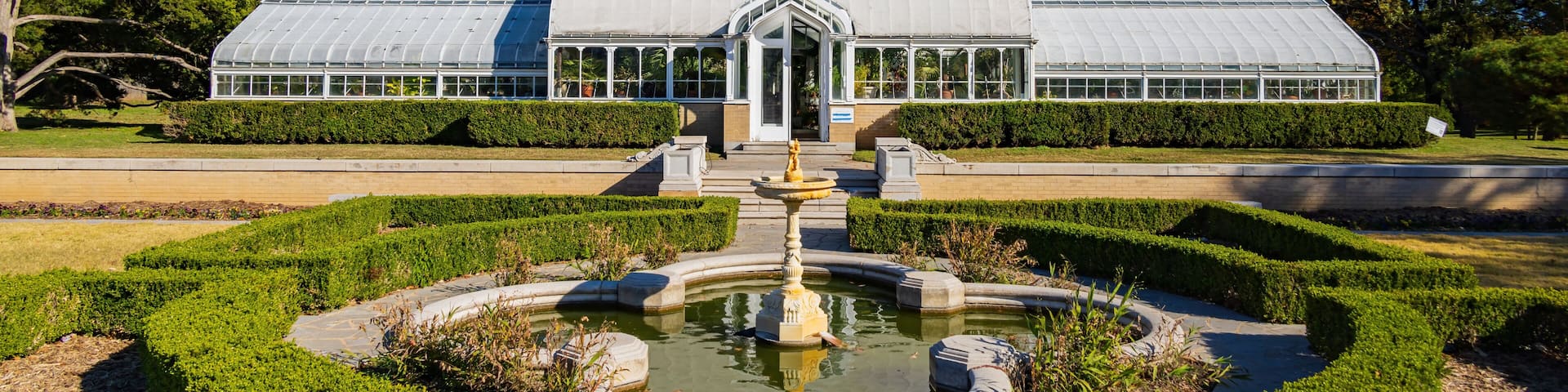 A greenhouse with a central fountain, surrounded by manicured hedges and trees.