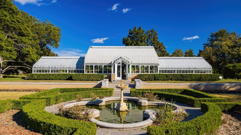 A greenhouse with a central fountain, surrounded by manicured hedges and trees.