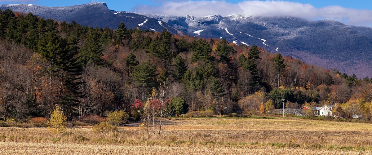 A mountainous landscape with autumn foliage, a river, and a small house.