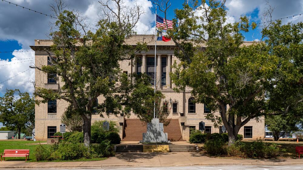 Un bâtiment historique, orné d’un mât pour drapeau, d’une statue et d’un banc rouge.