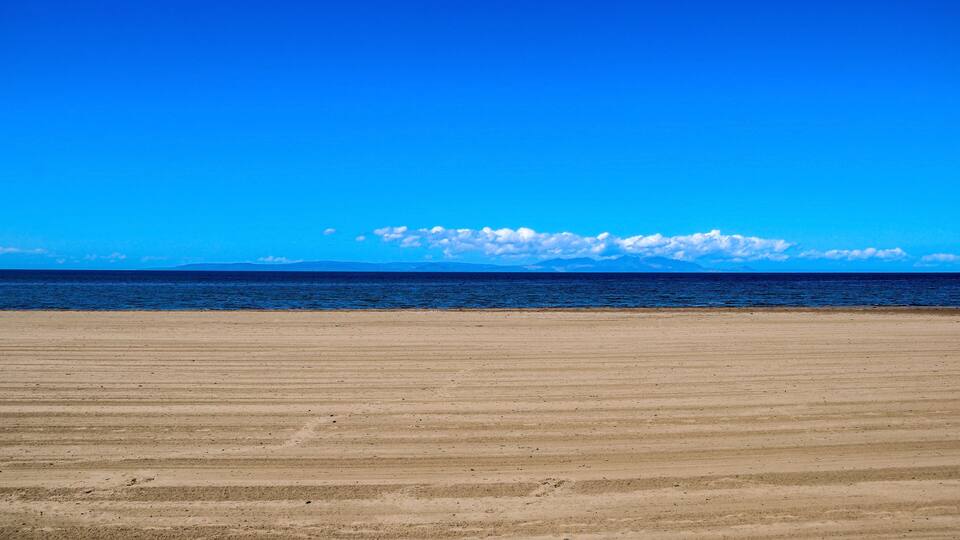 A wide sandy beach with a clear blue sky and calm ocean.