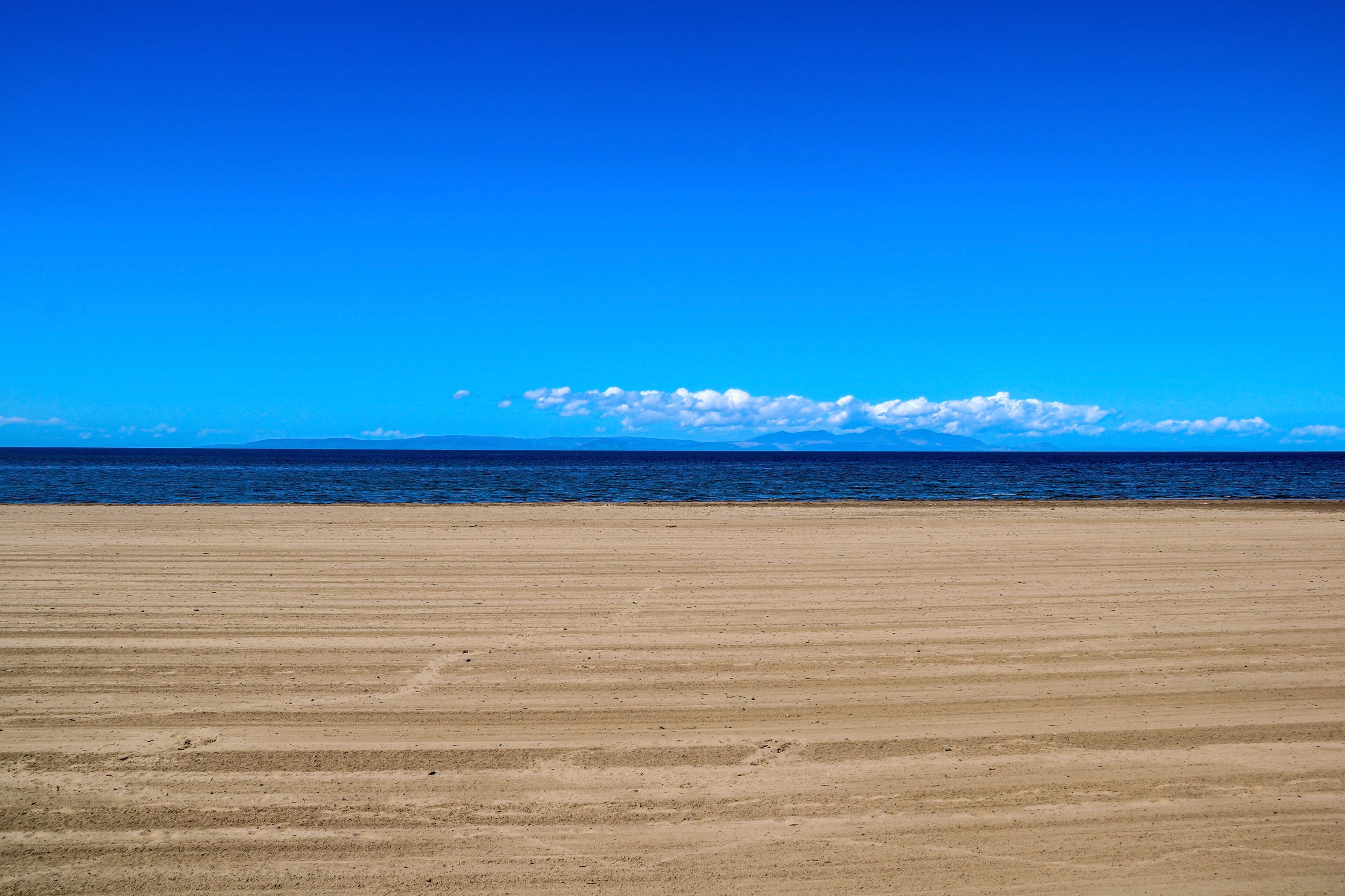 A wide sandy beach with a clear blue sky and calm ocean.