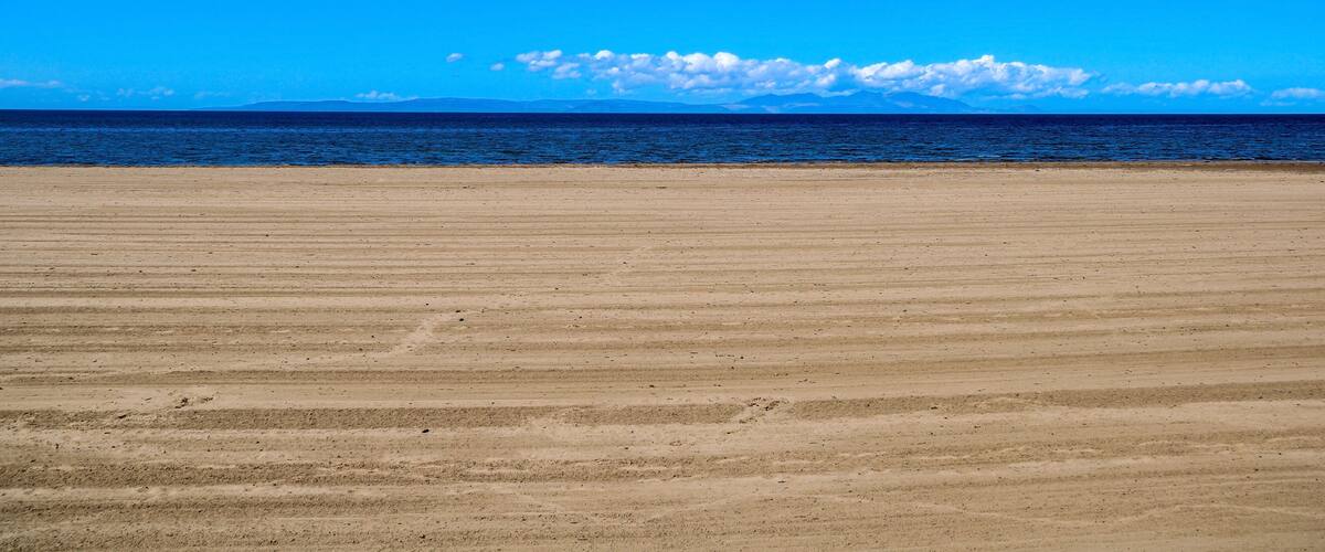 A wide sandy beach with a clear blue sky and calm ocean.