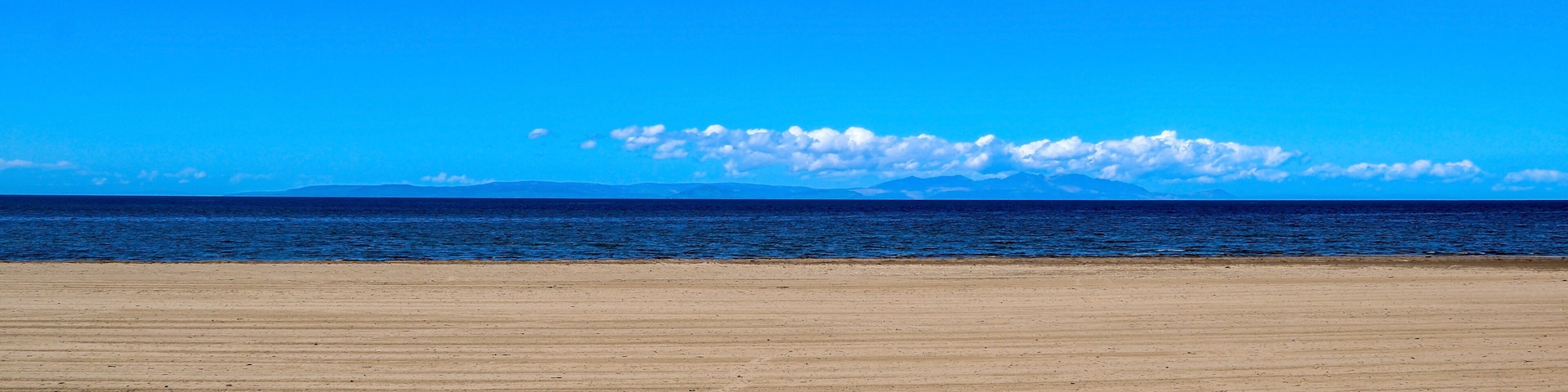 A wide sandy beach with a clear blue sky and calm ocean.