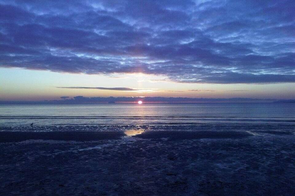 Um pôr do sol sobre uma praia com céu nublado.