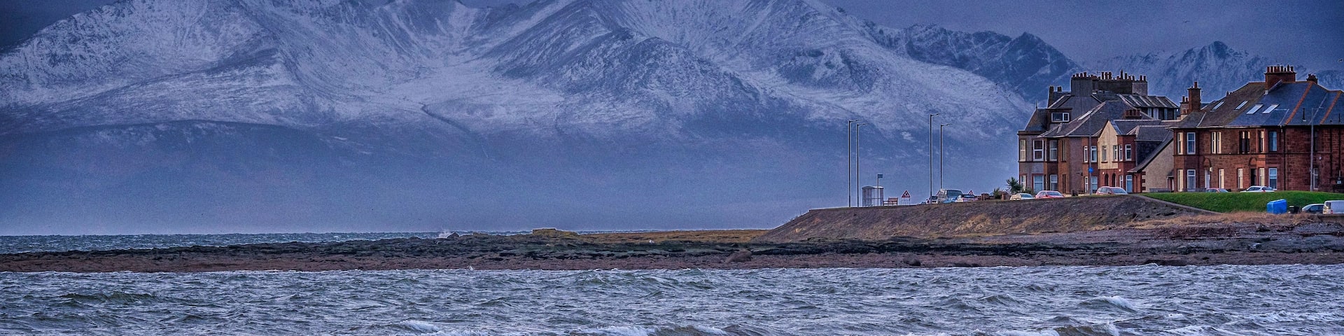 A beach with waves, a coastal building, and a mountain range in the background.