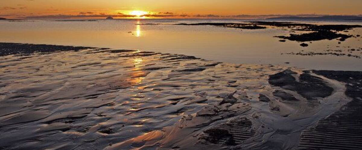Black Rocks, Troon Sunset on the Firth of Clyde with Ailsa Craig on the horizon to left of sun.