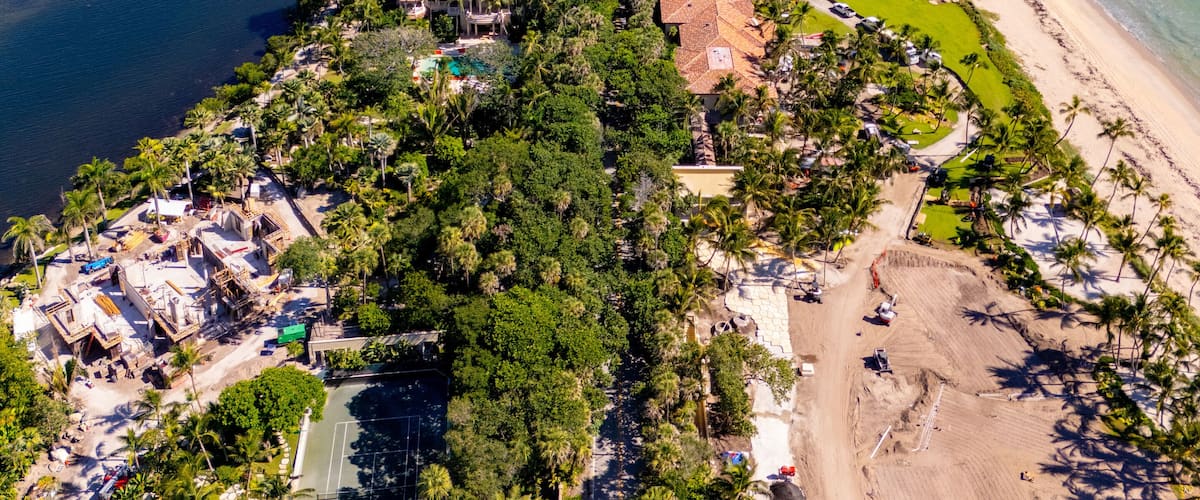 An aerial view of a coastal area with a beach, a marina, and lush greenery.