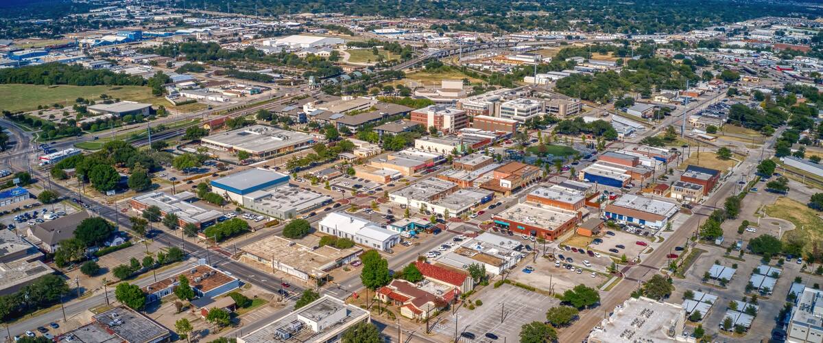 An aerial view of a city with a mix of commercial and residential buildings, roads, and green spaces.
