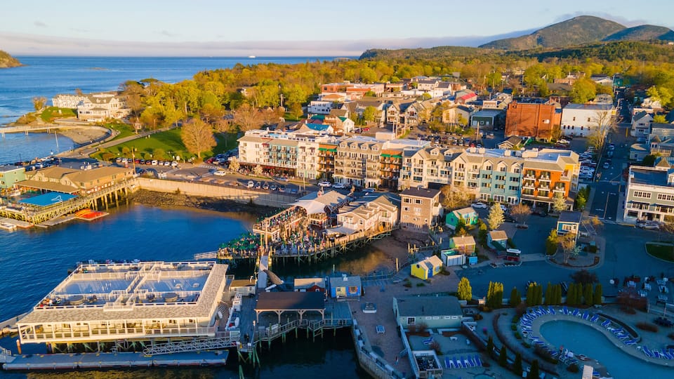 A coastal town with a marina, waterfront buildings, and a mountainous backdrop.