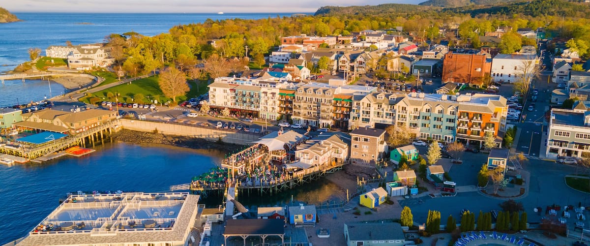 A coastal town with a marina, waterfront buildings, and a mountainous backdrop.
