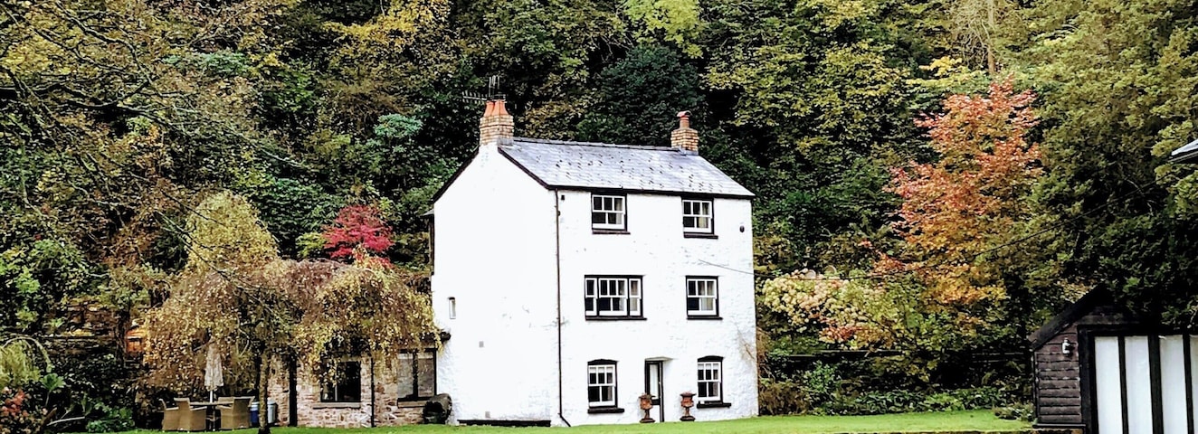 Uma casa branca refletida em águas calmas, rodeada por vegetação exuberante e árvores.