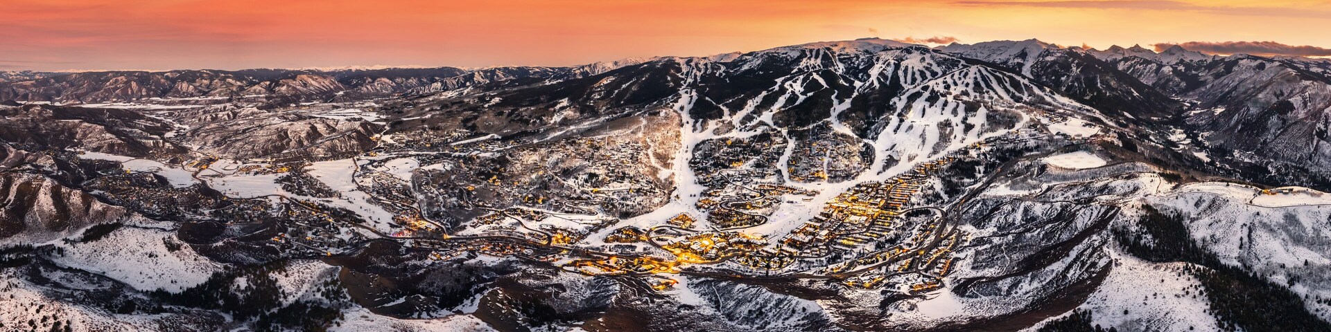 Un paisaje montañoso con un pueblo situado en un valle, rodeado de picos nevados.