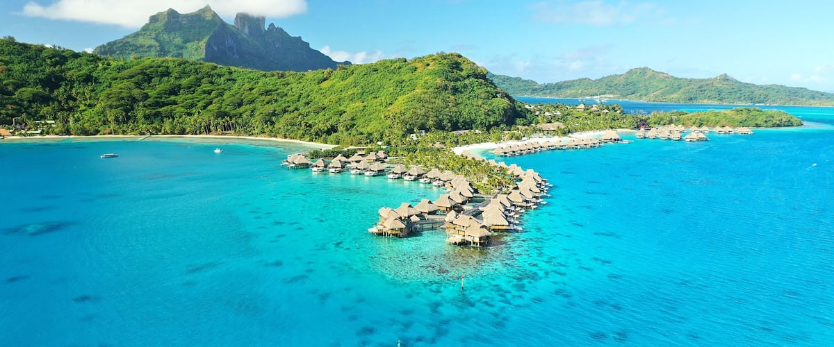 A tropical island with clear turquoise waters, overwater bungalows, and lush green mountains.