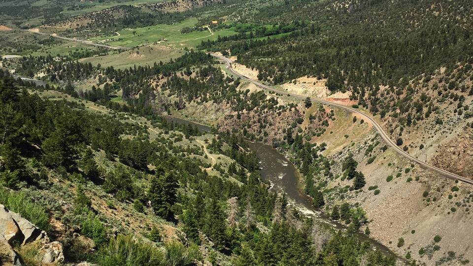 A valley with a winding river, surrounded by forested hills and a clear sky.