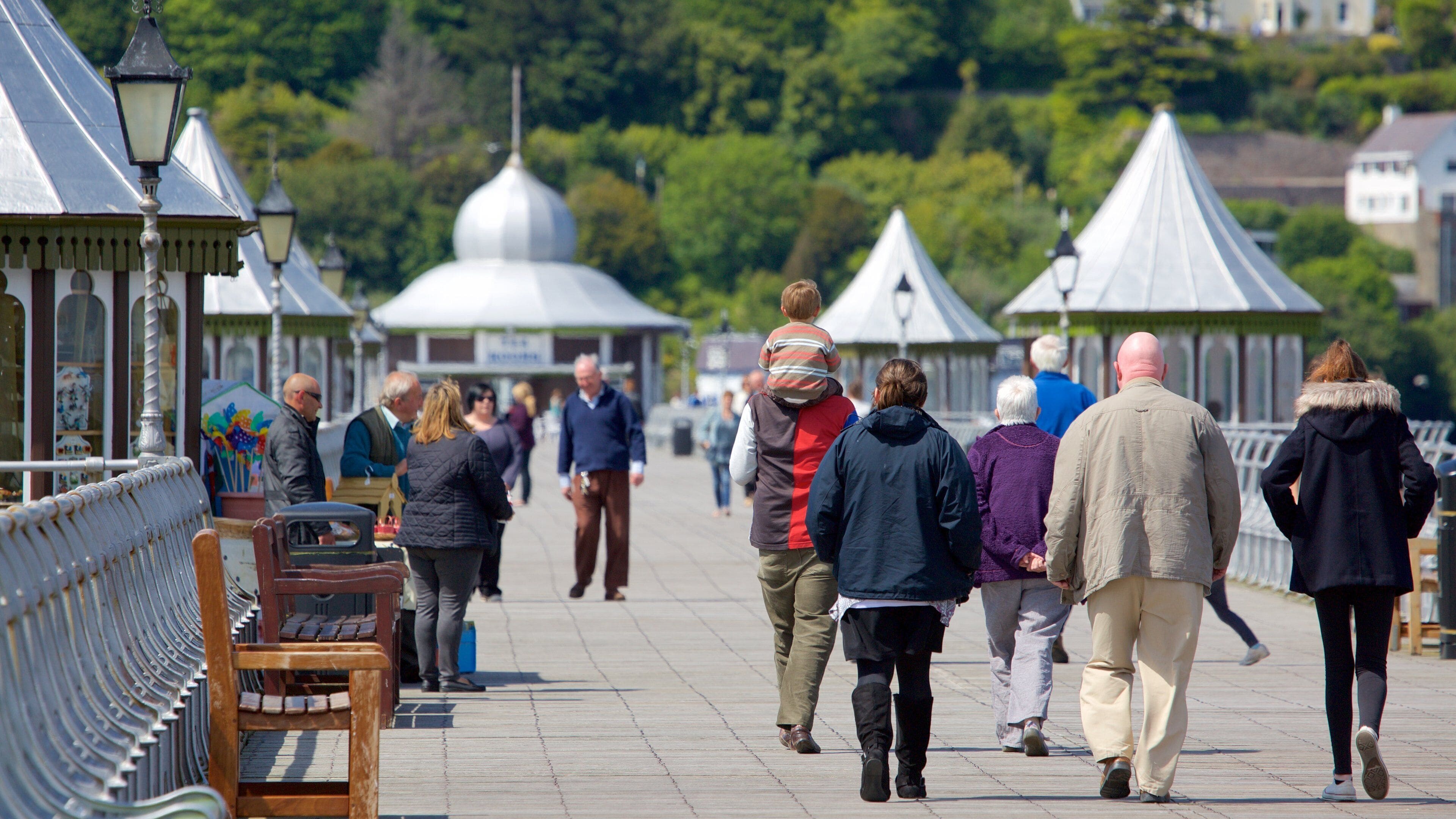 A promenade with people walking, metal lamp posts, and white domed structures in the background.