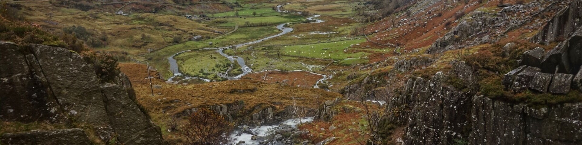 Un valle con un río, acantilados rocosos y campos verdes.