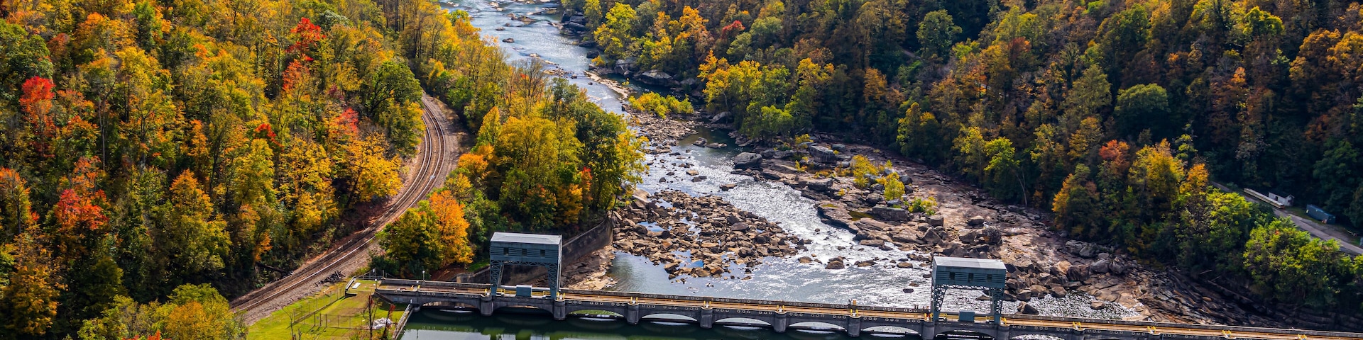 A river flowing through a forested valley with a bridge and a small building.