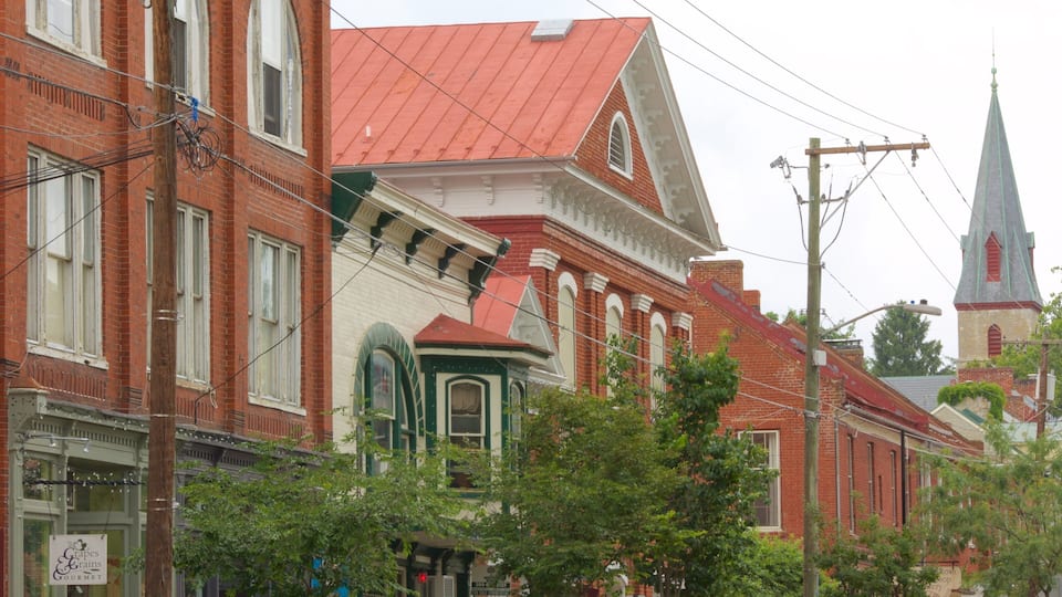 A historic street with red brick buildings, a church steeple, and a sign for a local shop.